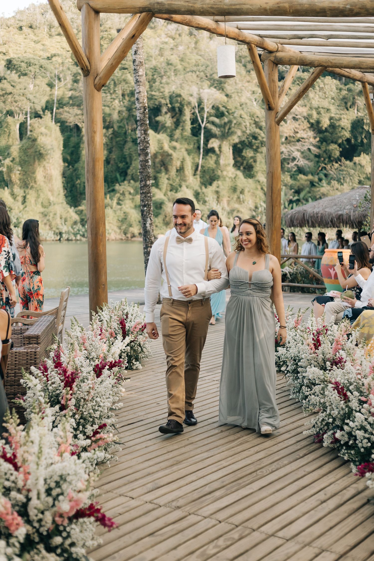Wedding attendants walking down a rustic wooden walkway adorned with pink and white flowers.