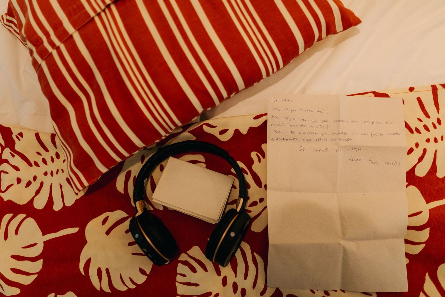 Red and white striped pillow with headphones and note paper on floral print fabric.