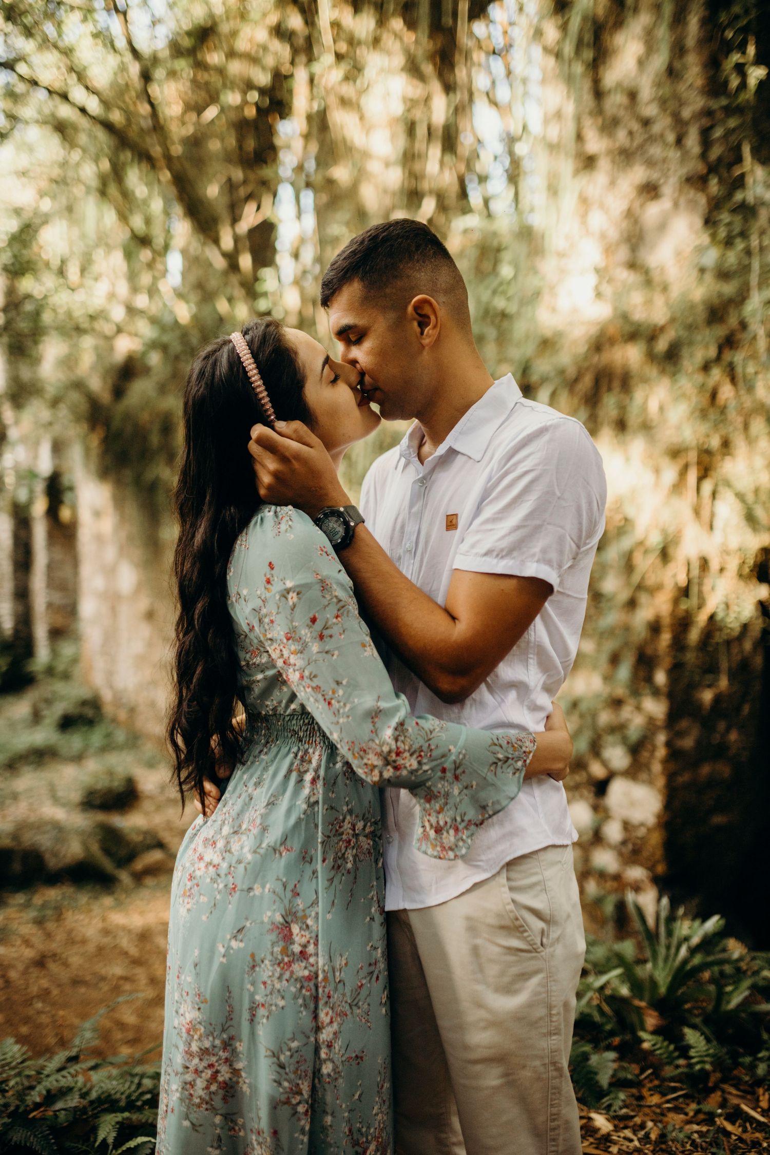 Couple in coordinated white and mint outfits sharing an intimate moment in a wooded setting.