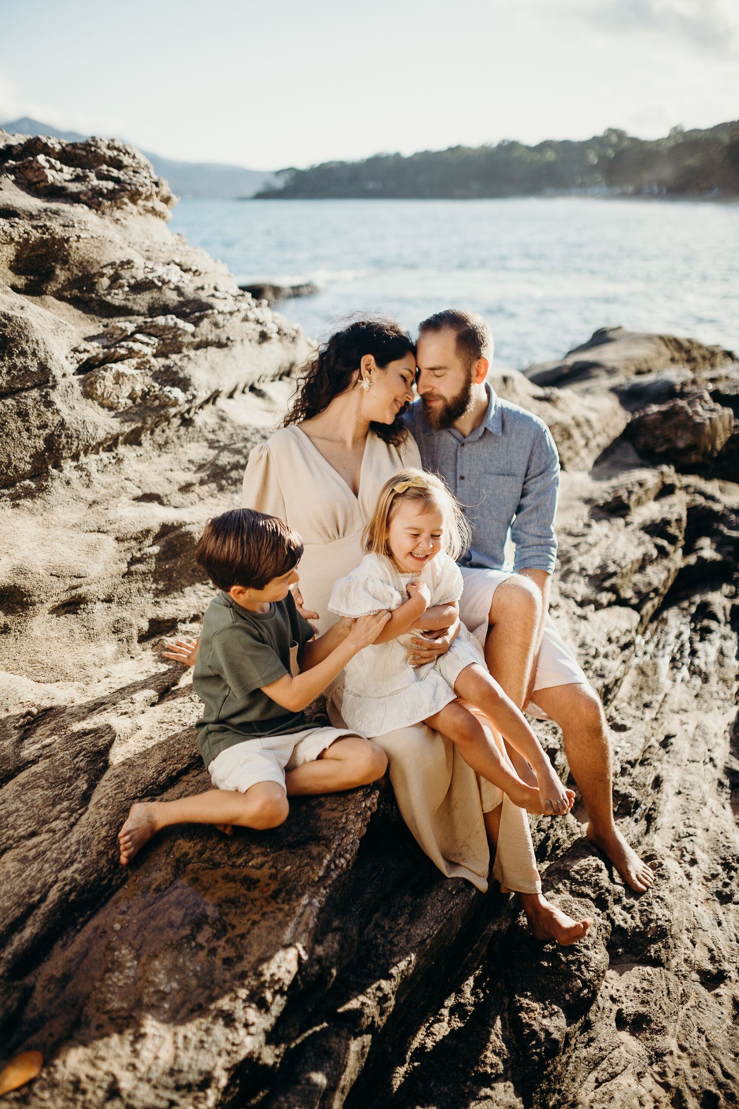 An intimate family portrait captured on rugged oceanside rocks during a sunny afternoon.