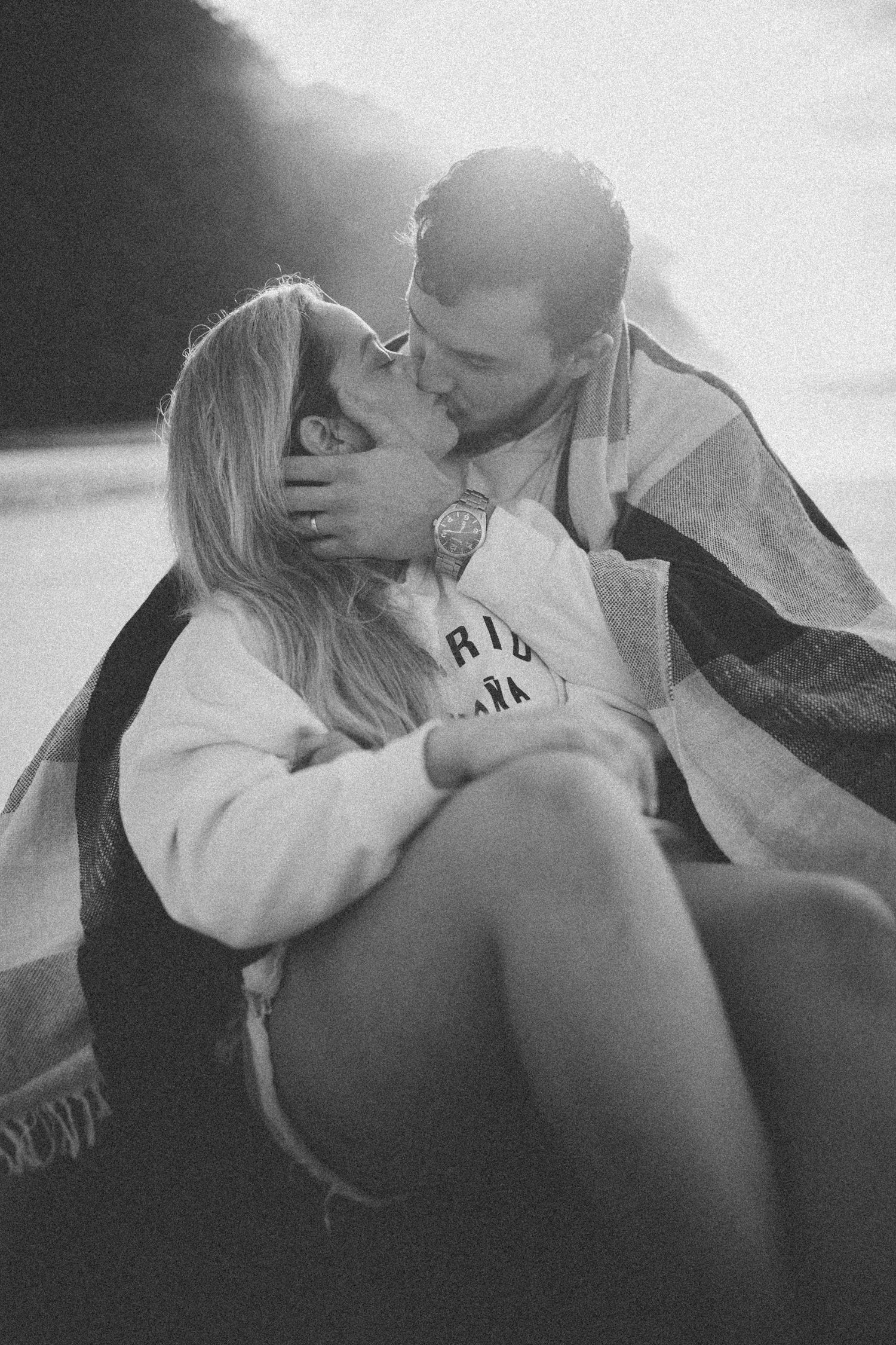 A black and white candid photo capturing a tender moment between a couple on the beach.