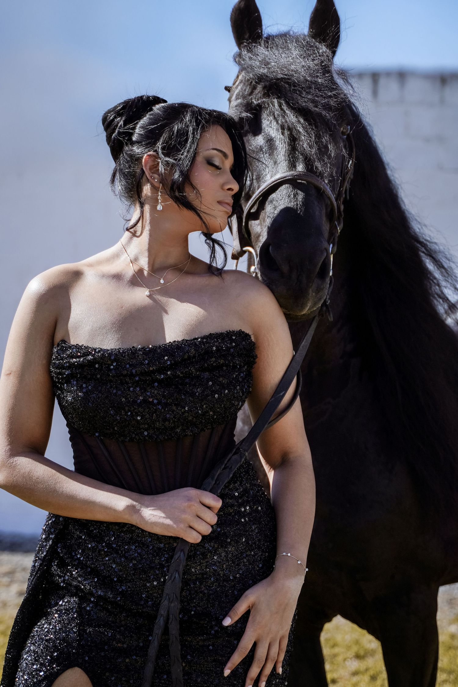 Woman in black strapless sequin gown standing close to a black horse.