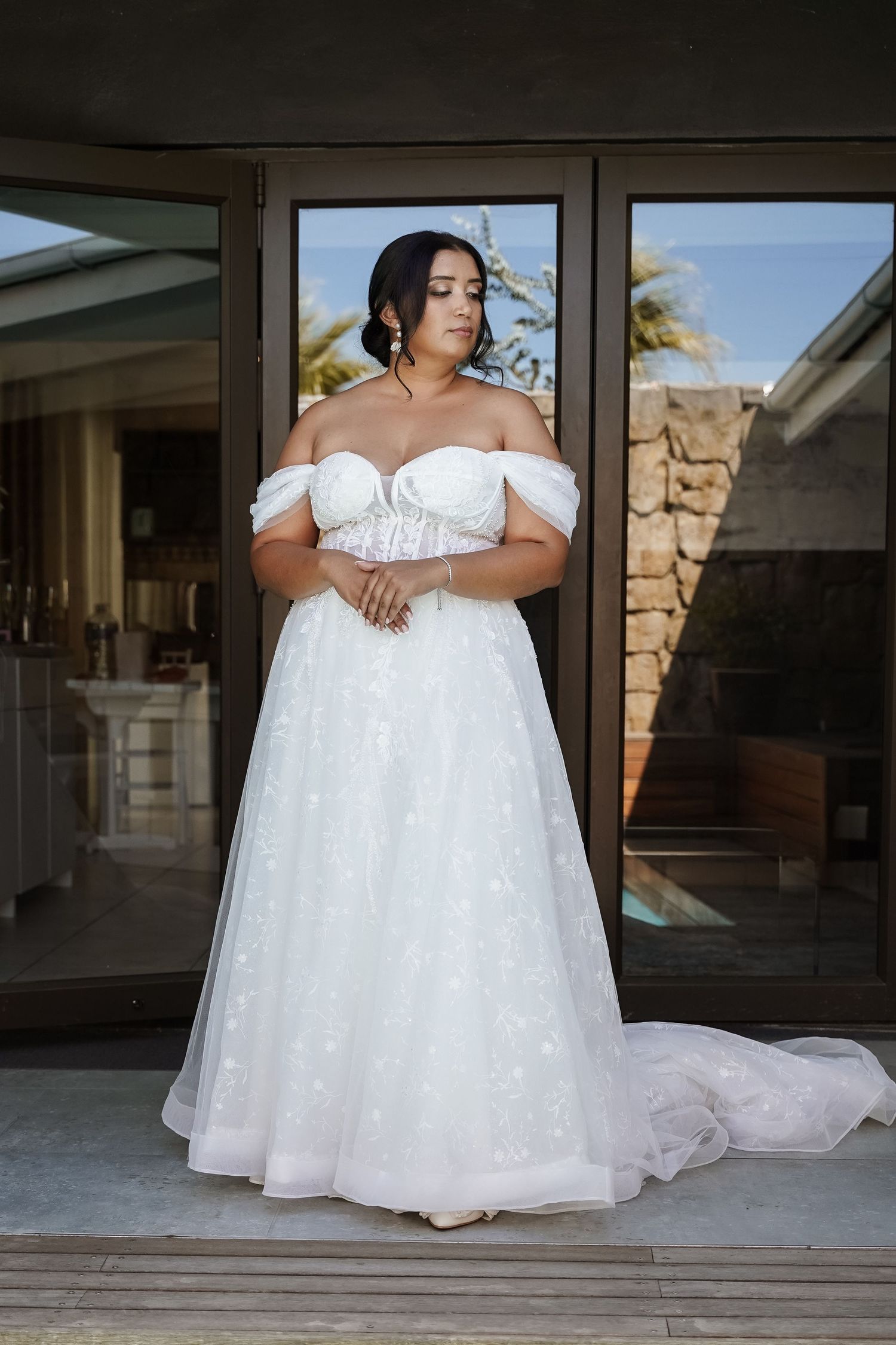 Plus-size bride in off-shoulder white A-line wedding gown with sparkle tulle, posing outdoors.