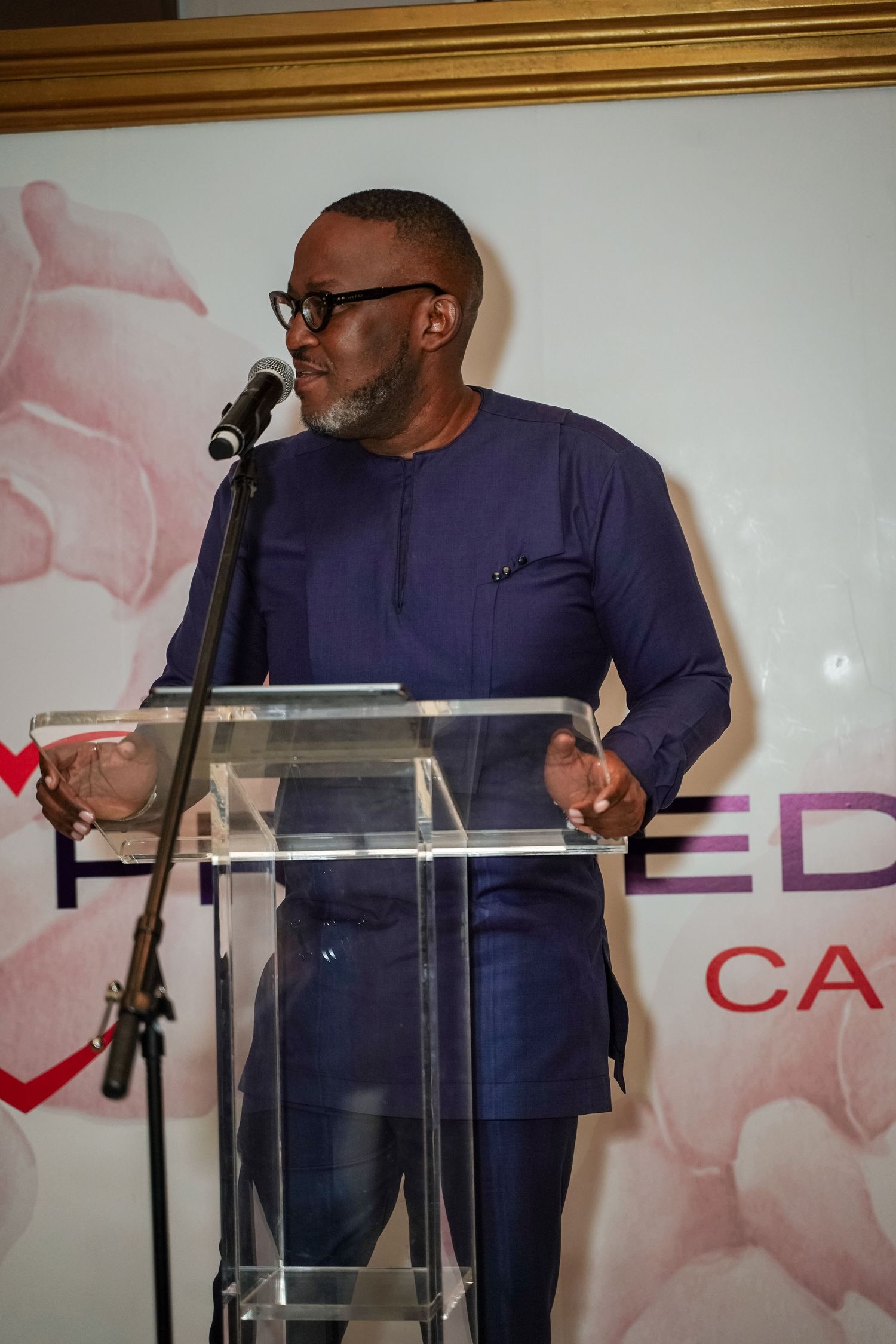 Man in navy African attire speaking at a podium at a Primedia Cares event.