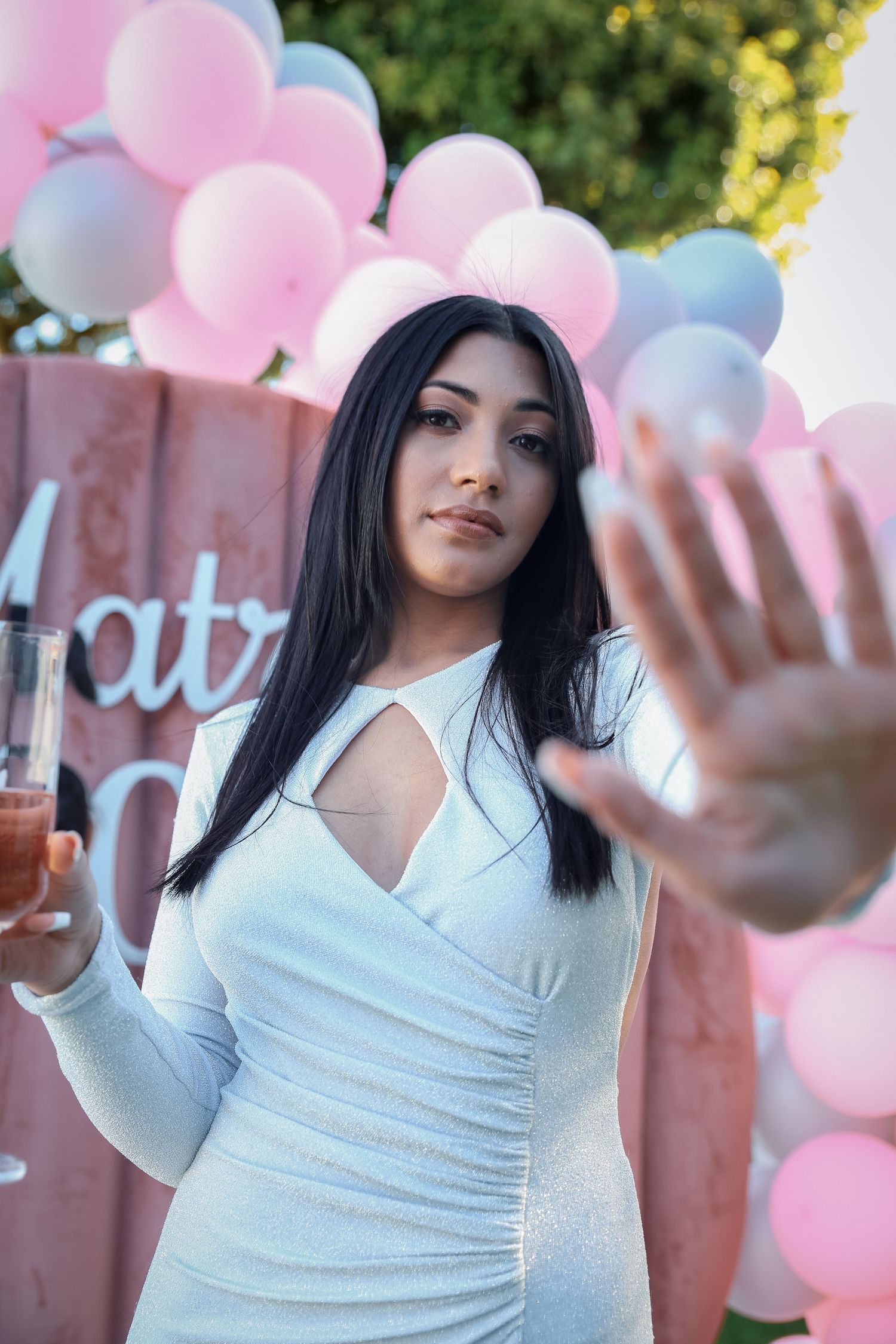 Woman in white cutout dress reaching toward camera at outdoor Matric party with pink balloons.