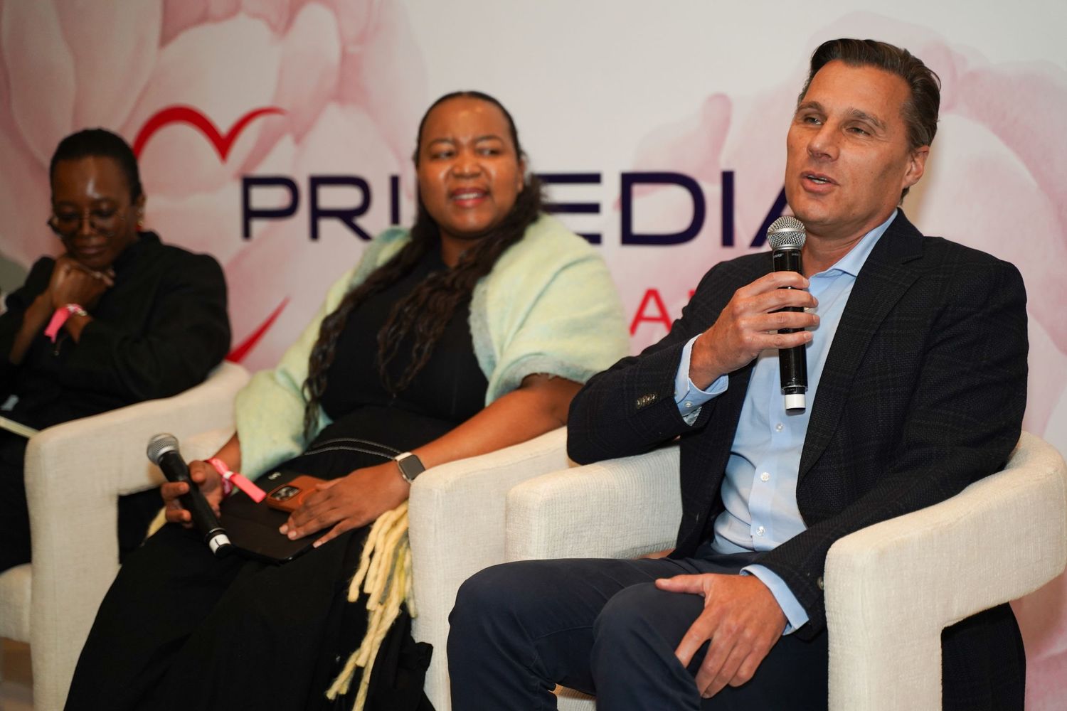 Panel of three people speaking at a Primedia Cares event seated on white chairs.