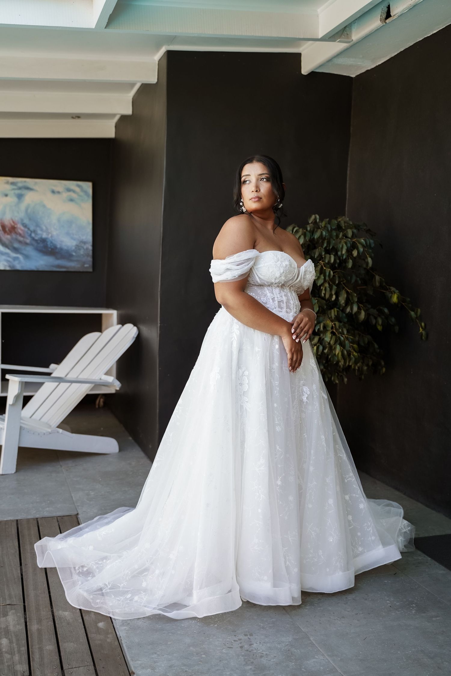 Plus-size bride wearing an off-shoulder white ball gown wedding dress with floral lace details and a flowing train.