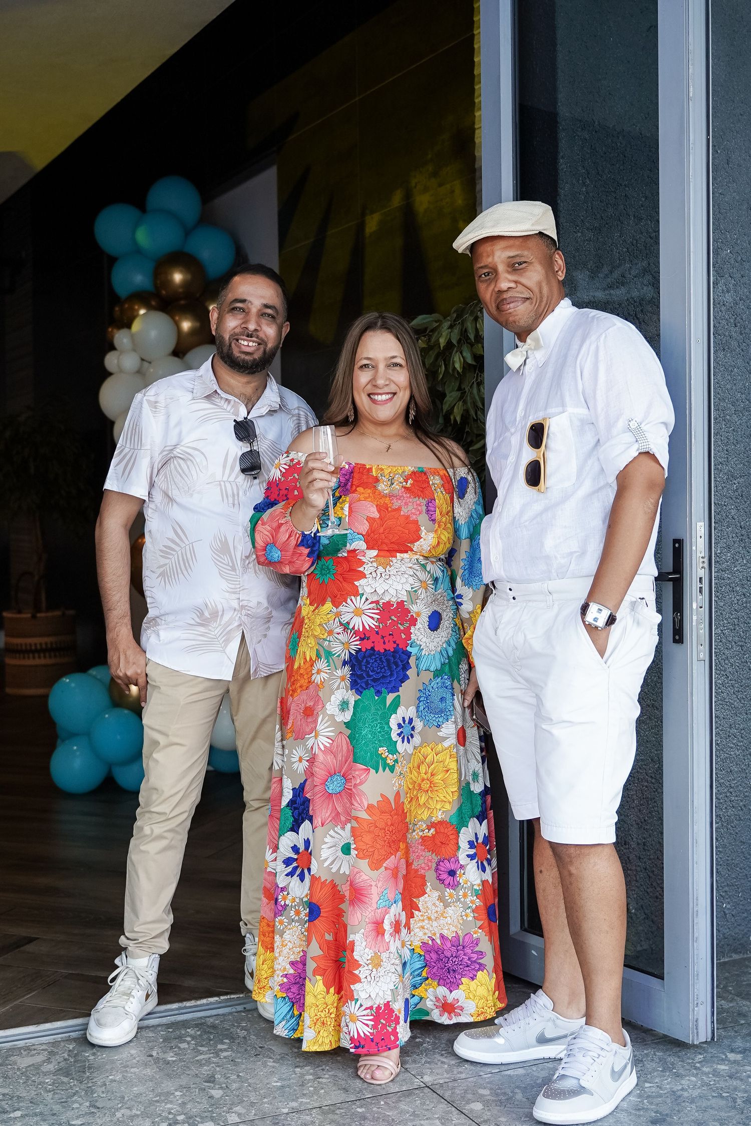 Three people posing together at celebration event with colorful balloons in background.