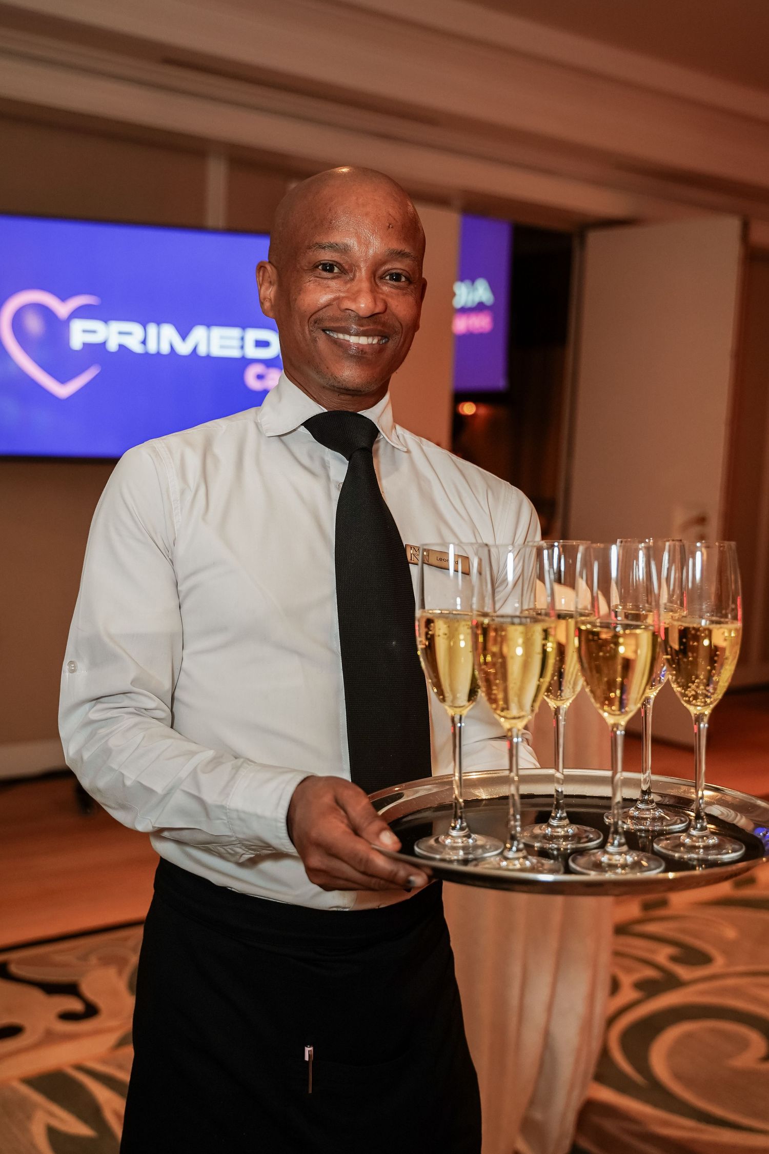 Cheerful waiter holding tray of champagne flutes at Primedia Cares corporate gala.