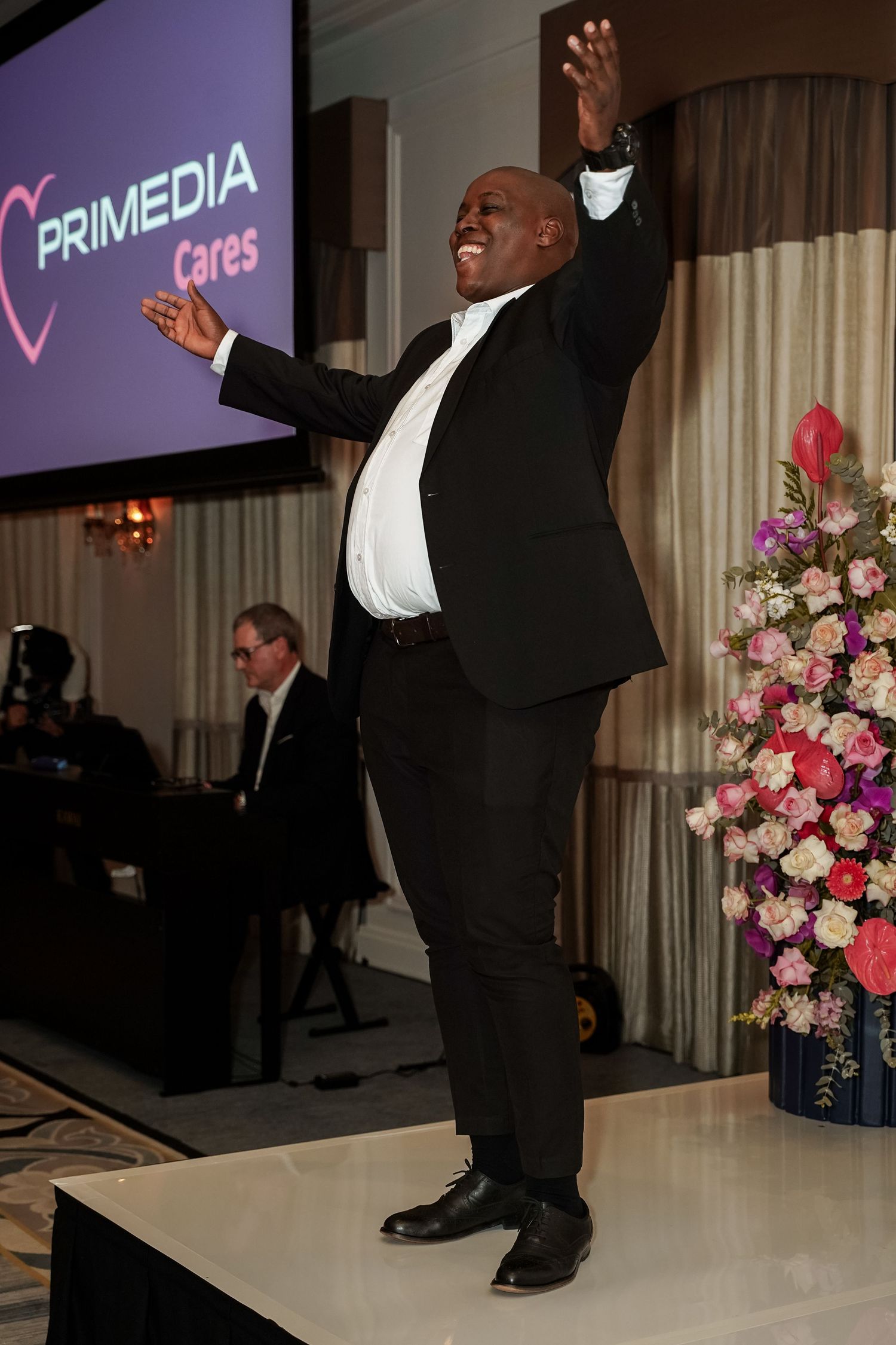 Man in tuxedo celebrating on stage at a Primedia Cares event.