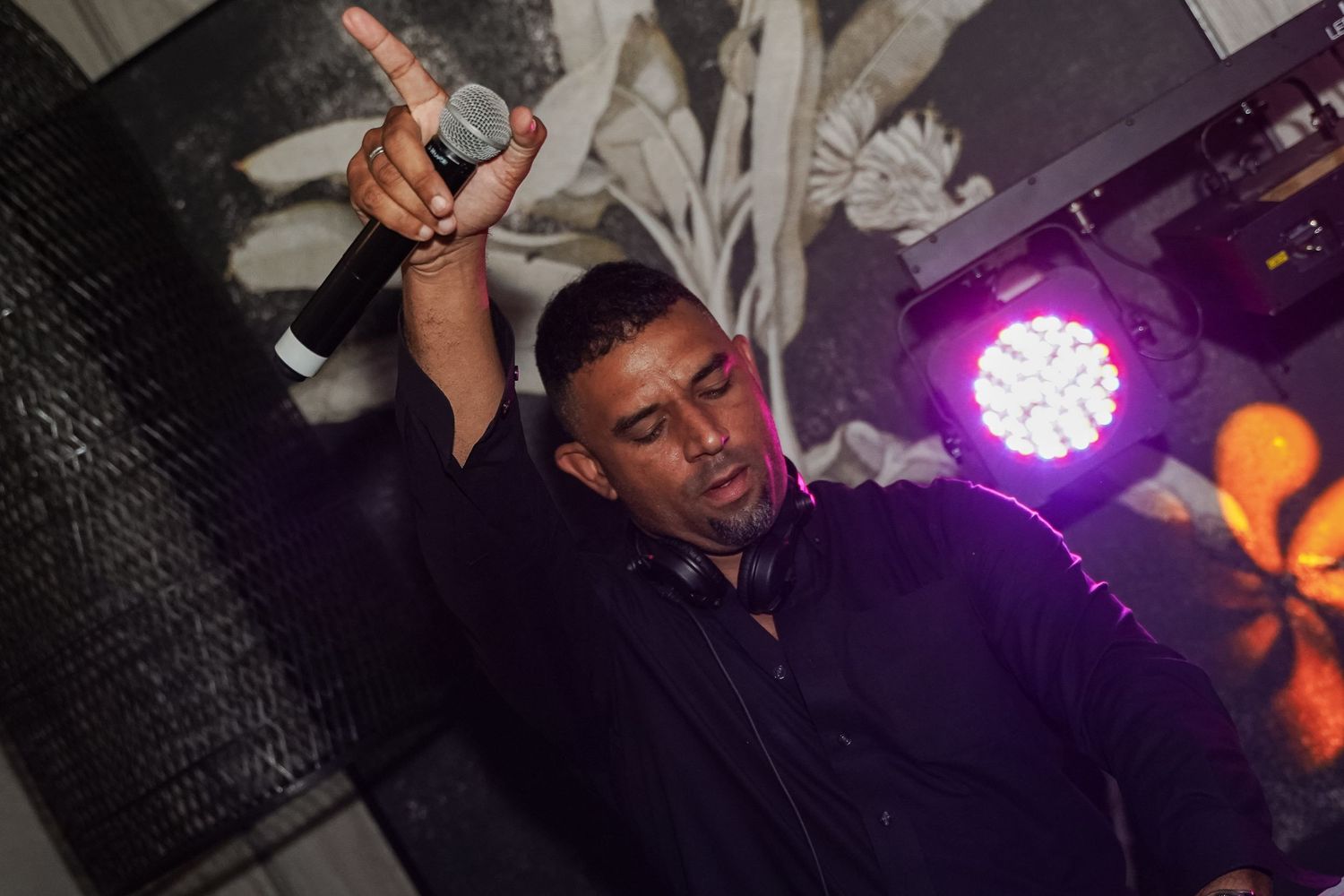 DJ performing on stage holding microphone up with purple stage lighting behind him.
