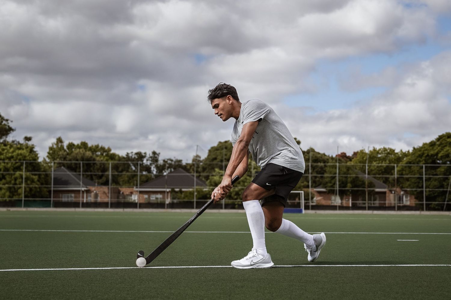 Male field hockey player in grey shirt striking a ball on an artificial turf pitch.