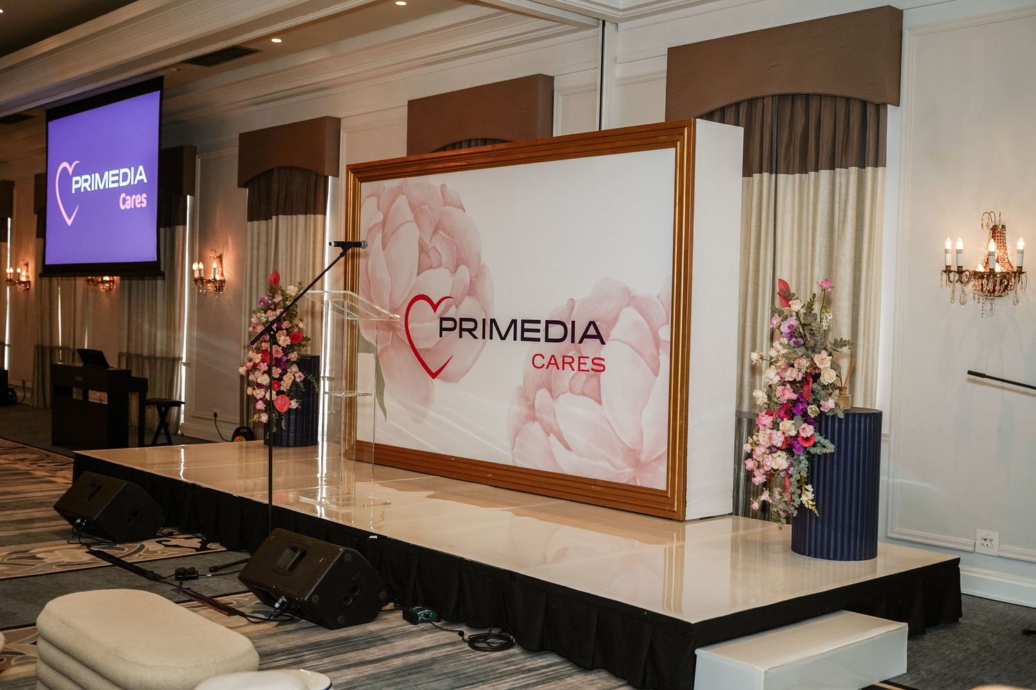 Primedia Cares event stage with floral arrangements and branded backdrop in elegant ballroom.