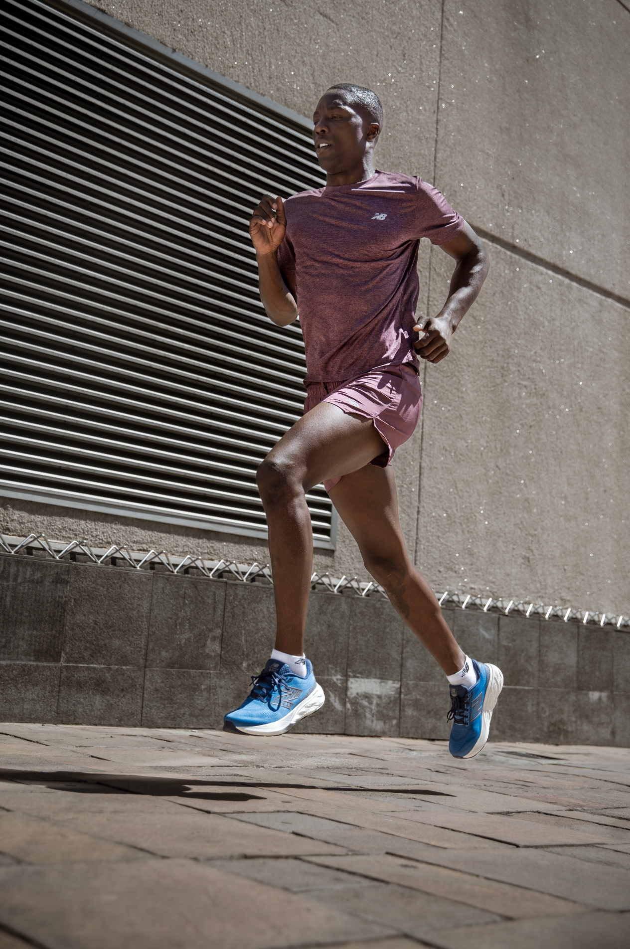 Male athlete running in pink sportswear and blue sneakers outdoors.