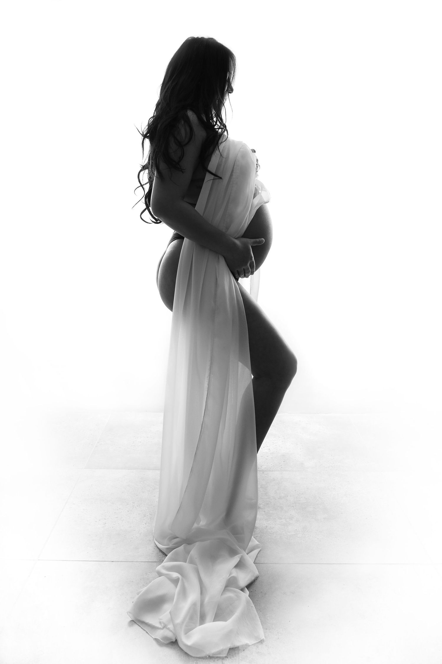 Elegant black and white silhouette of a pregnant woman with long hair wrapped in flowing sheer white fabric.