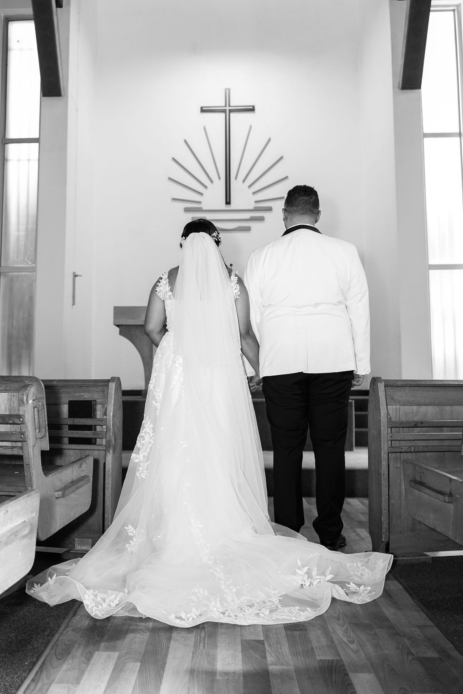 Black and white photo of bride and groom standing at church altar before a cross during wedding ceremony.
