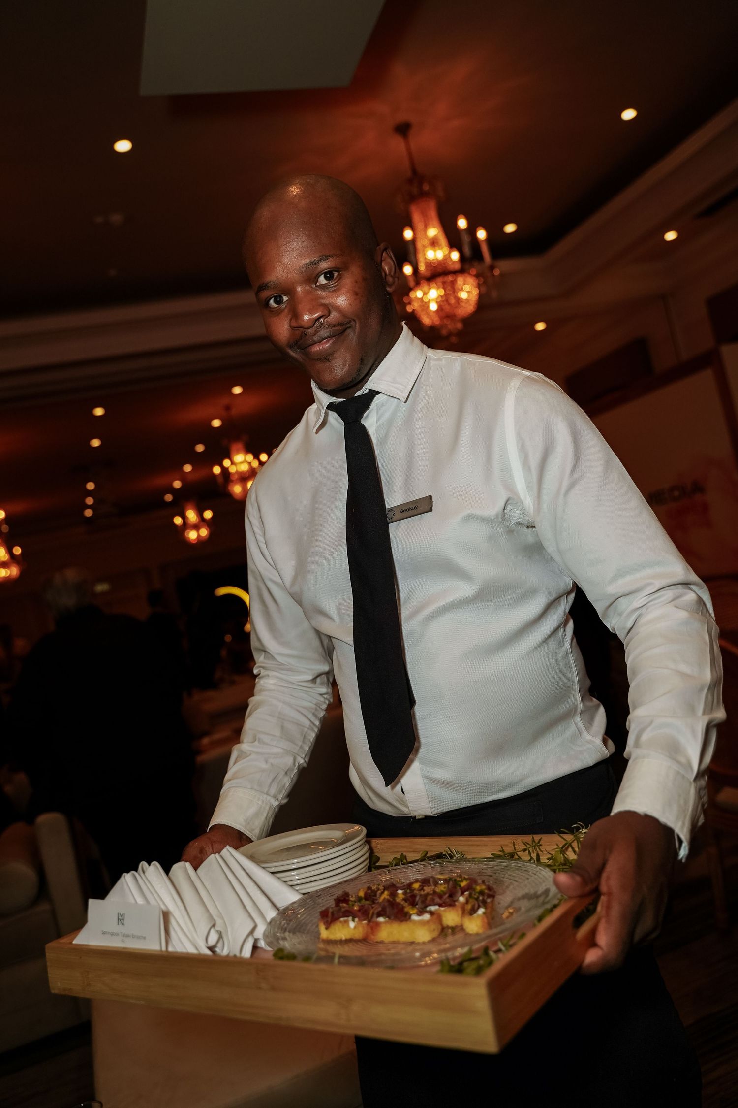 Friendly waiter presenting food platter on wooden board at Primedia Cares event.