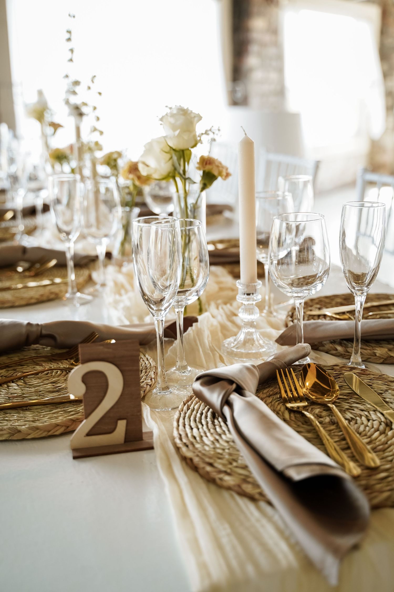 Elegant gold and white wedding table setting with crystal glasses, gold cutlery, and floral centerpiece.