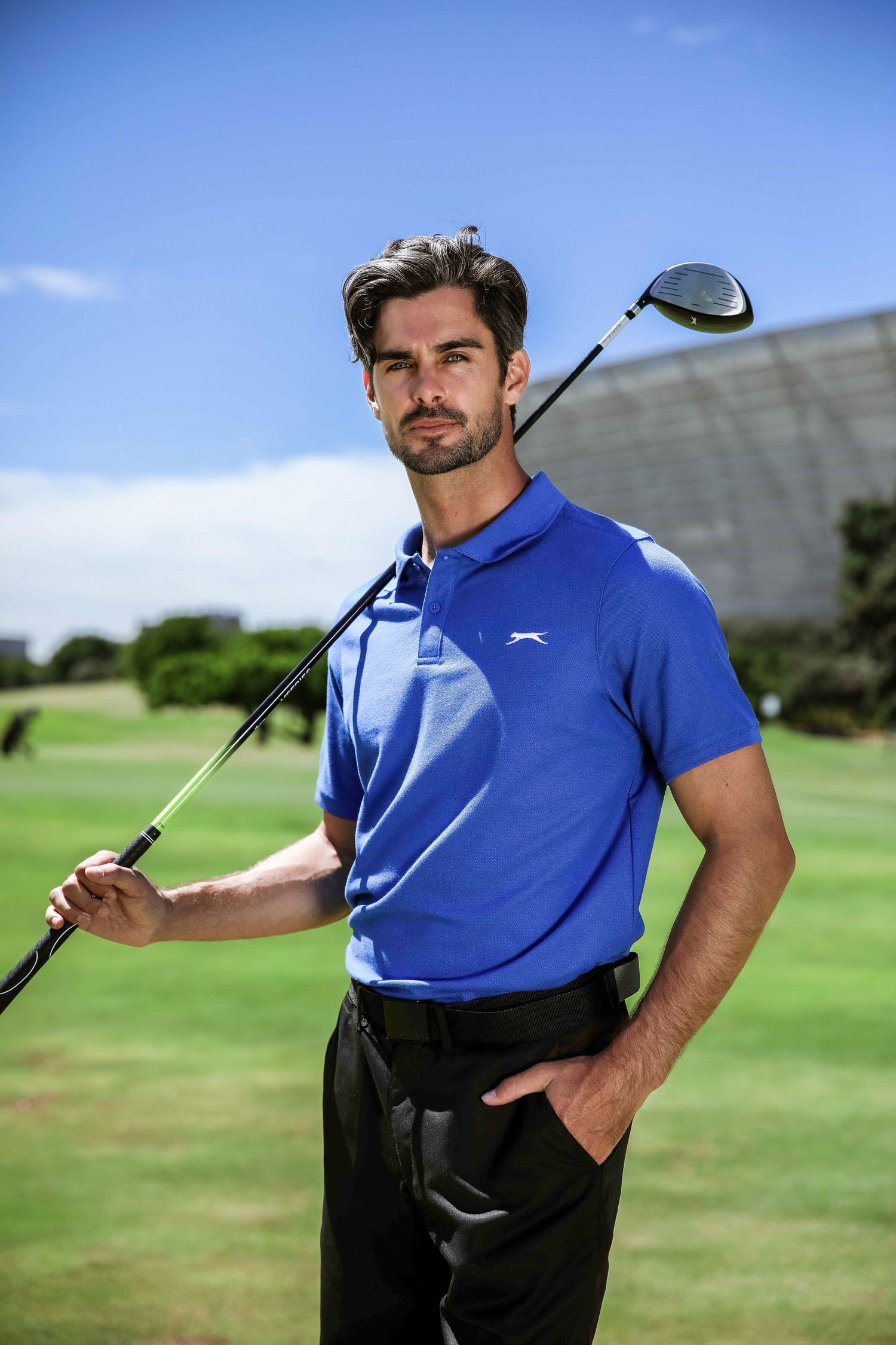 Man in blue Slazenger polo shirt holding a golf club on a sunny golf course.