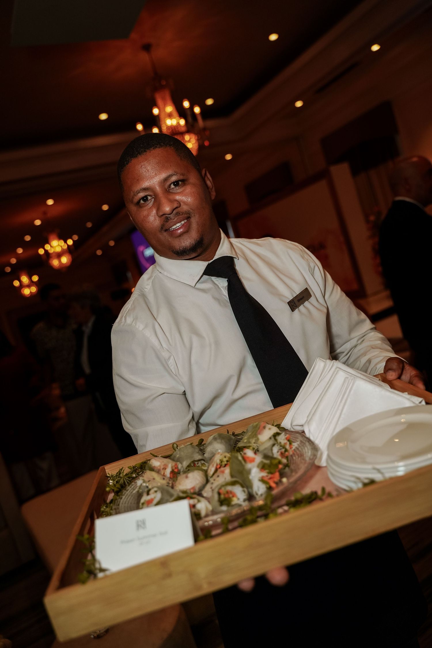 Smiling waiter presenting tray of canapes at Primedia Cares corporate event.
