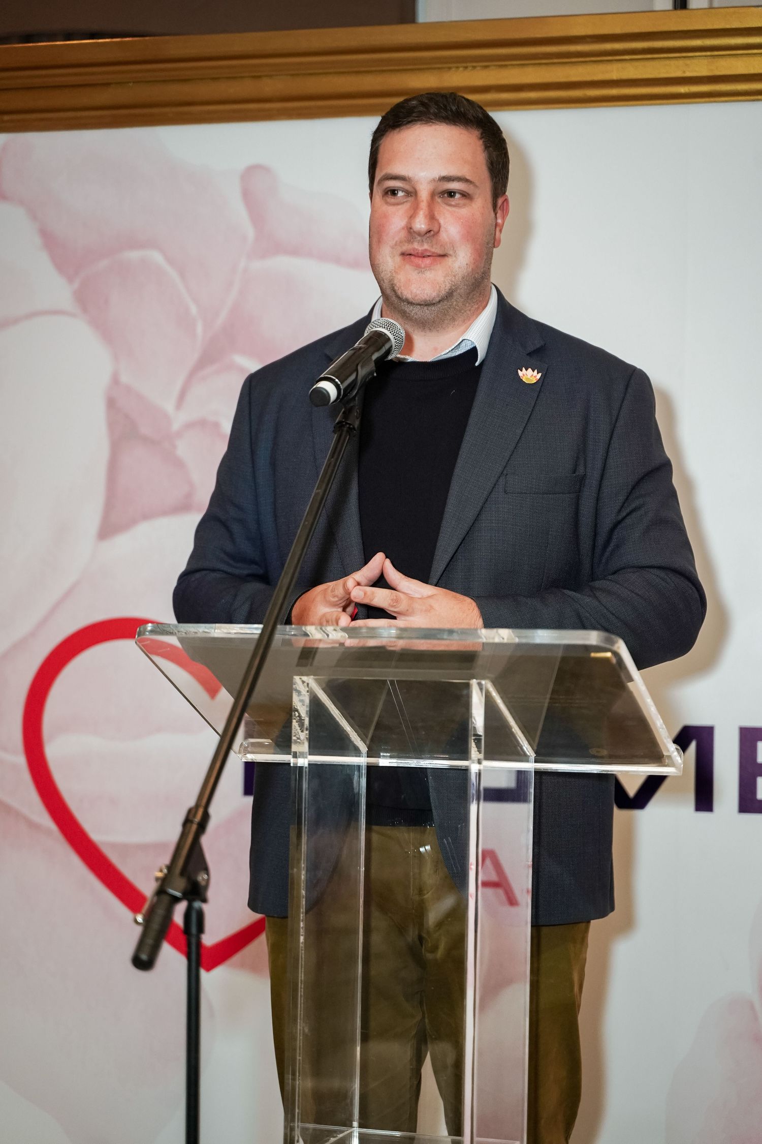 Man in blazer speaking at a glass podium at a Primedia Cares event.