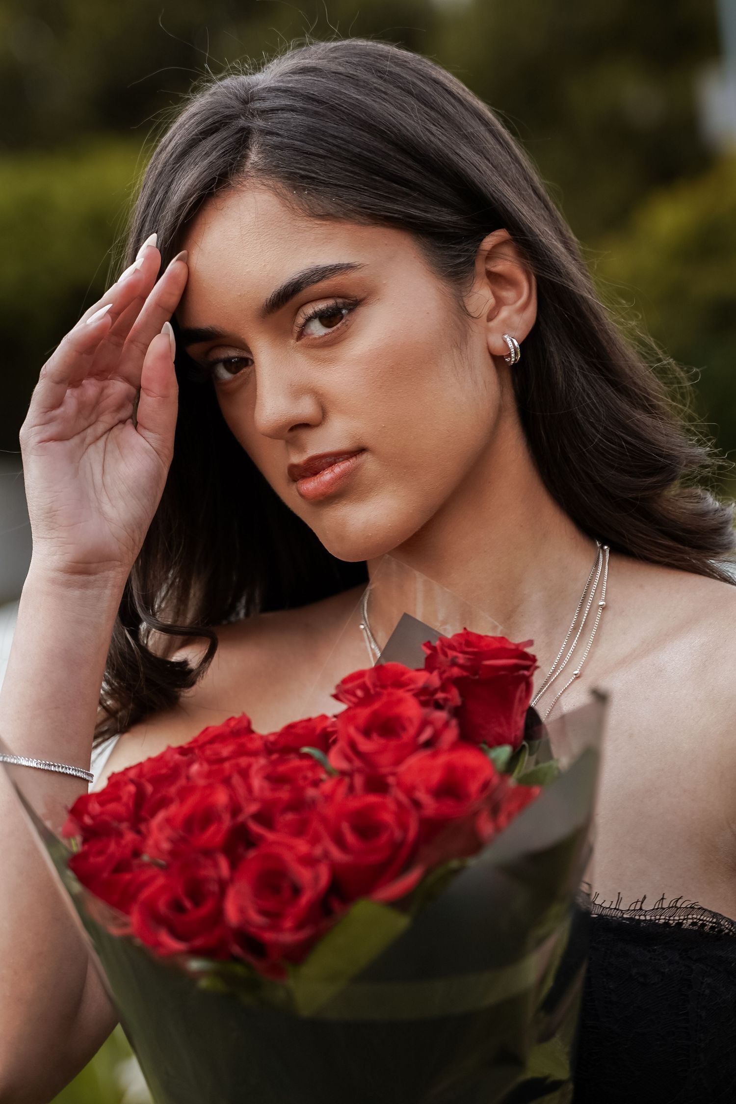 Close-up portrait of young woman with red rose bouquet touching her forehead wearing silver jewelry.