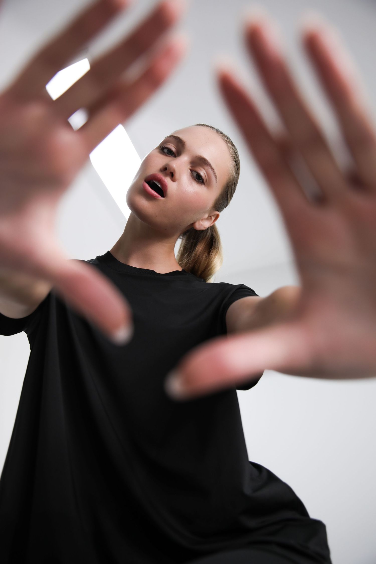 Woman in black t-shirt reaching toward camera with both hands on white background.