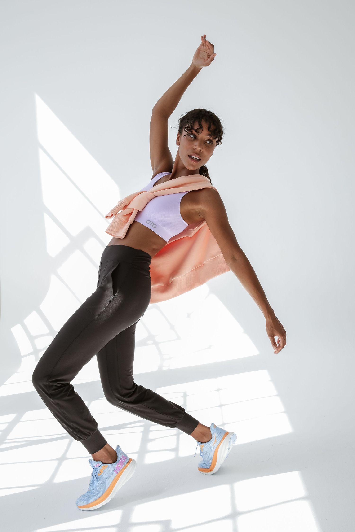 Athletic Black woman in colorful sports top and black joggers jumps dynamically in bright white studio.