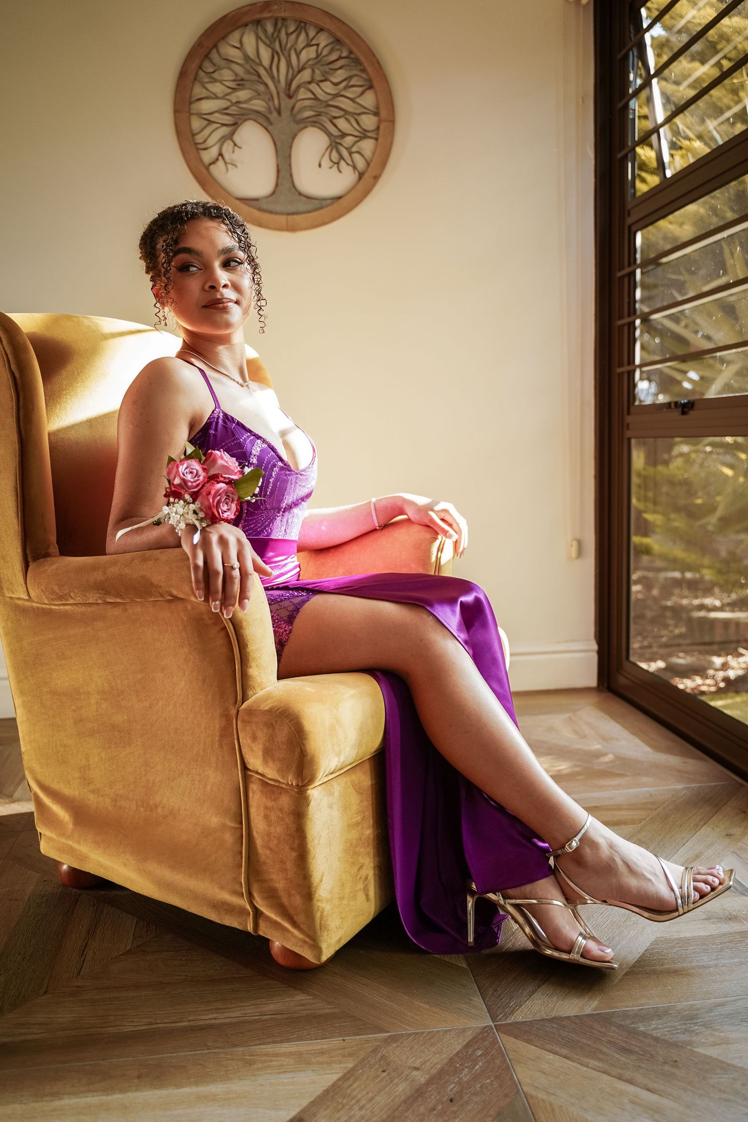 Young woman in purple satin gown seated in gold velvet armchair holding flowers.