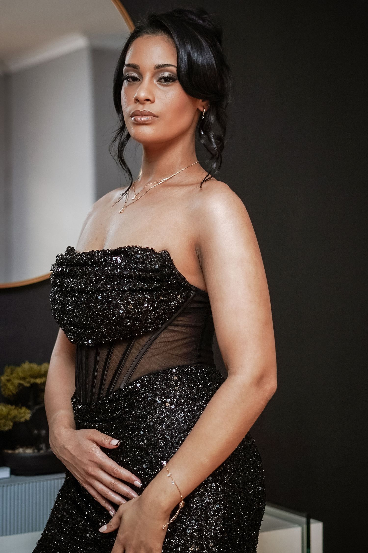 Young woman in black strapless sequin corset gown posing indoors.