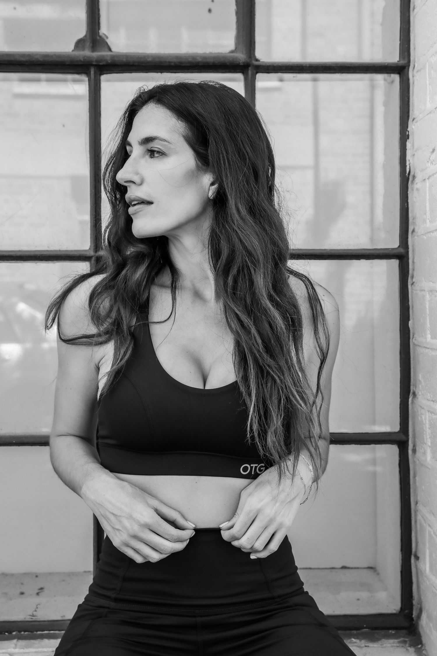 Fit woman with long dark hair wearing black OTG sports bra poses in black and white fitness photo.