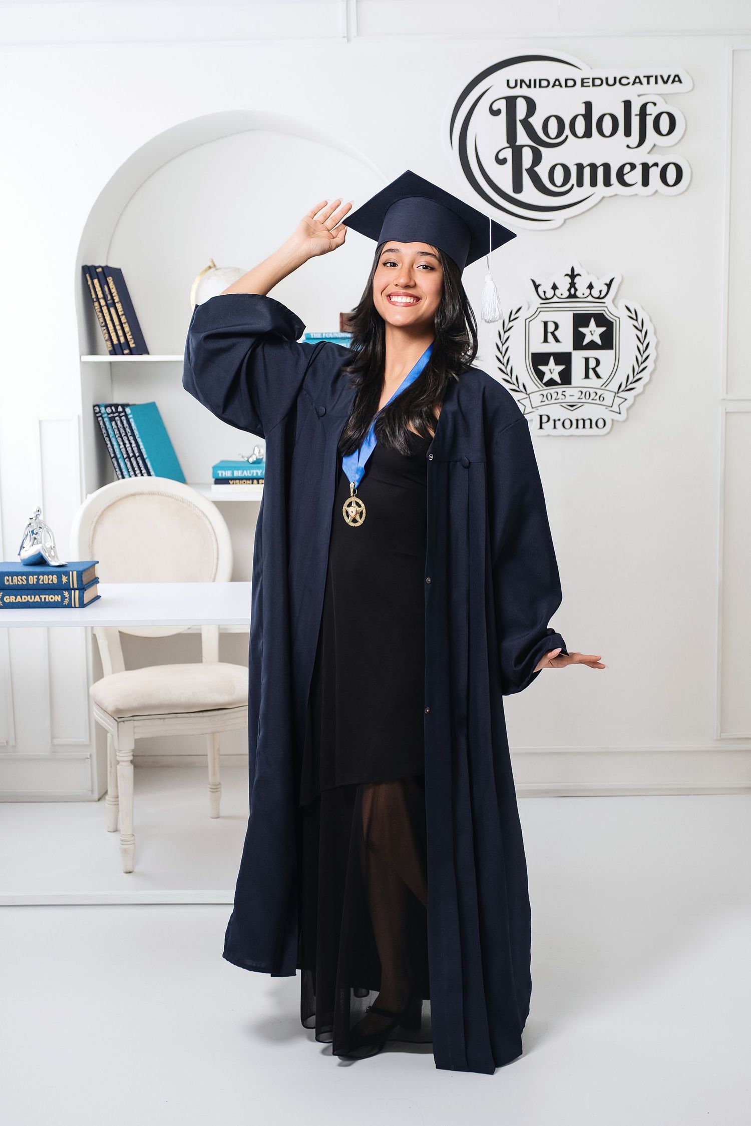 Smiling graduate in navy cap and gown with medal at Unidad Educativa Rodolfo Romero graduation ceremony.