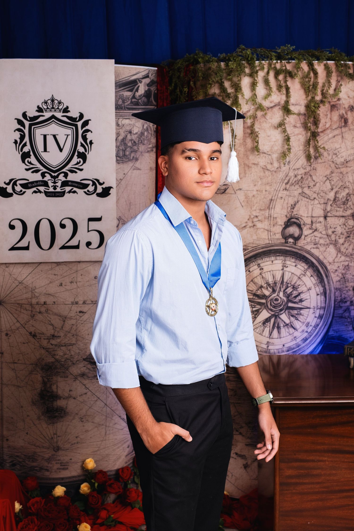Young man in graduation cap and medal poses proudly before a 2025 backdrop with compass design.