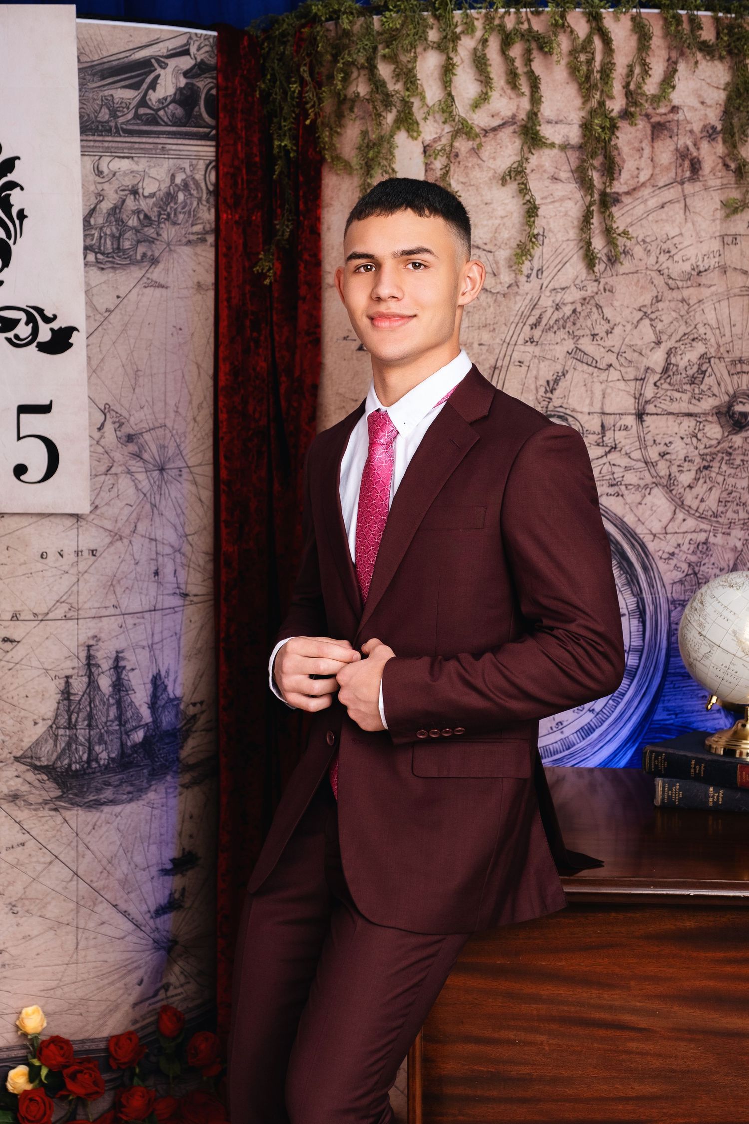 Young man in burgundy suit and pink tie poses confidently in front of a vintage map backdrop.