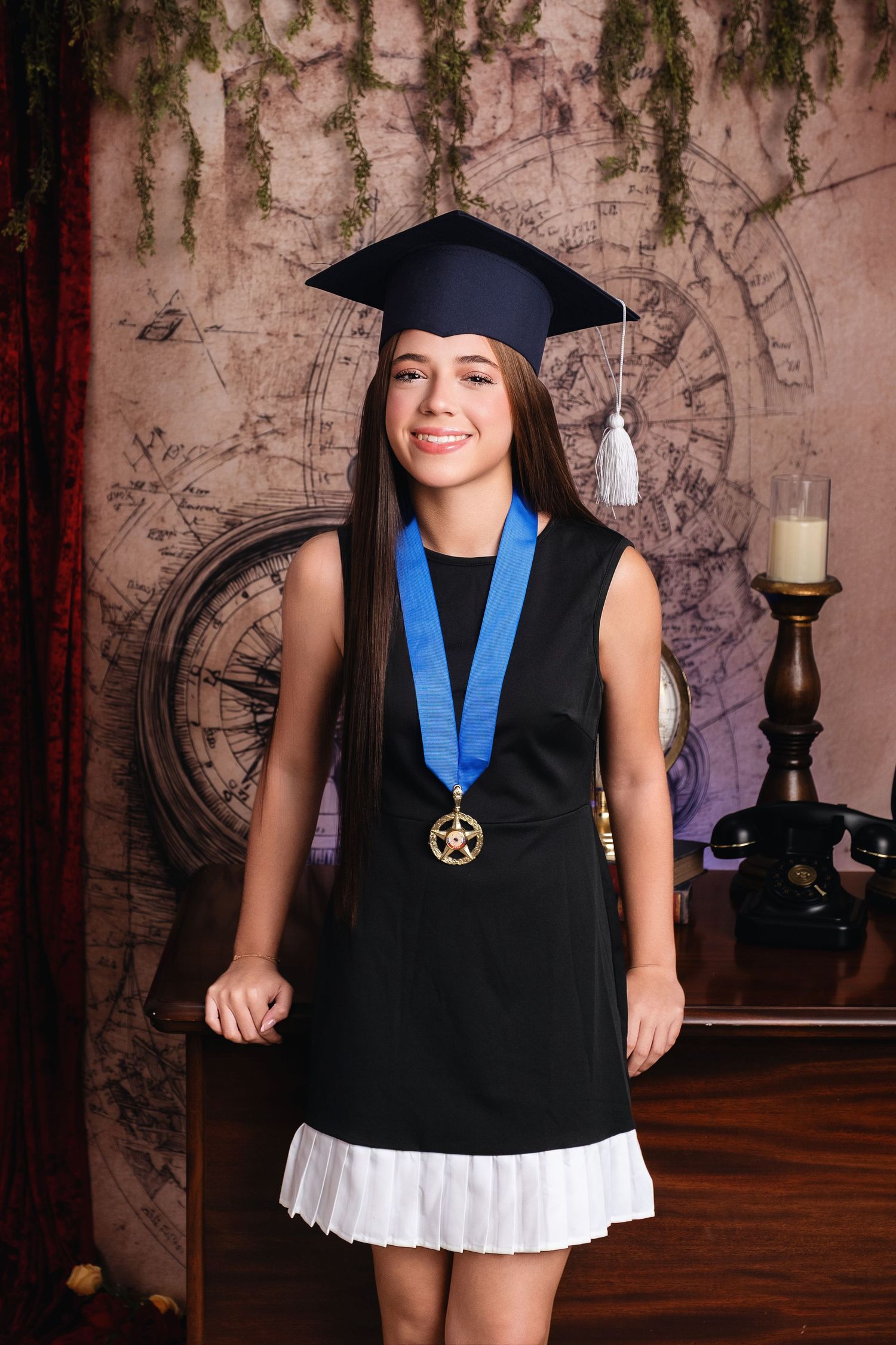 Young girl in graduation cap and gown with gold star medal on blue ribbon smiling for portrait photo.