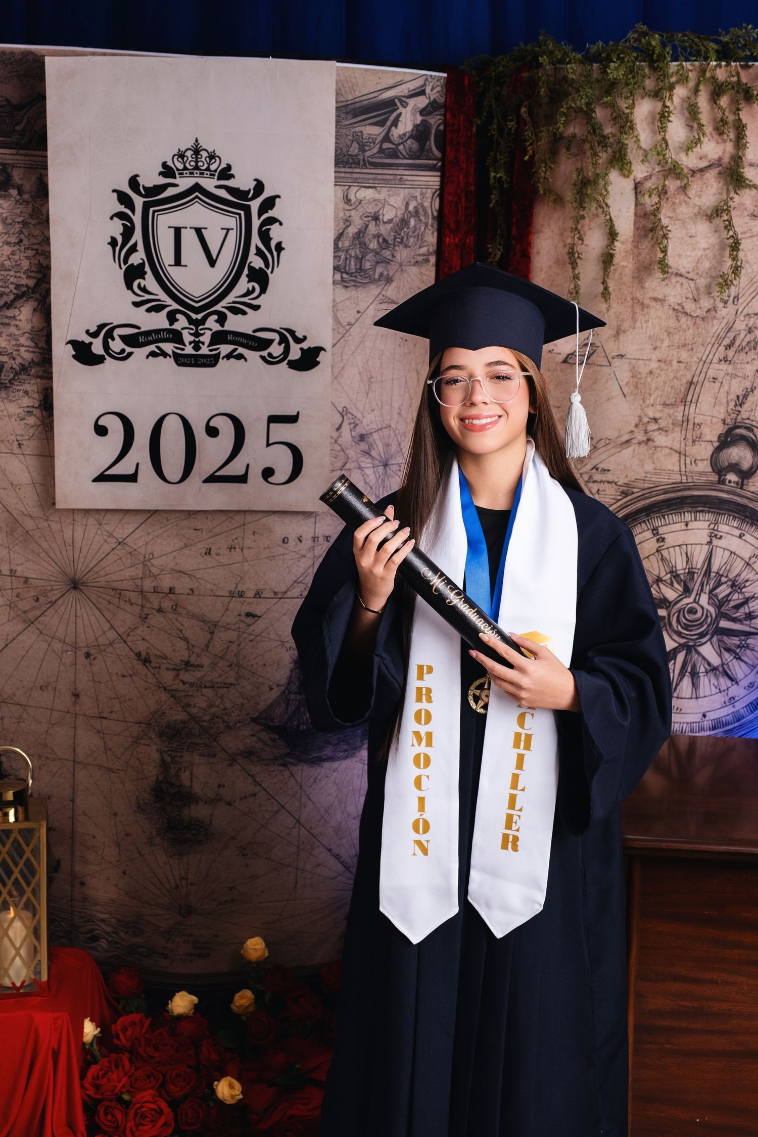 A smiling graduate in cap and gown holds a diploma tube and stole at a 2025 graduation ceremony.