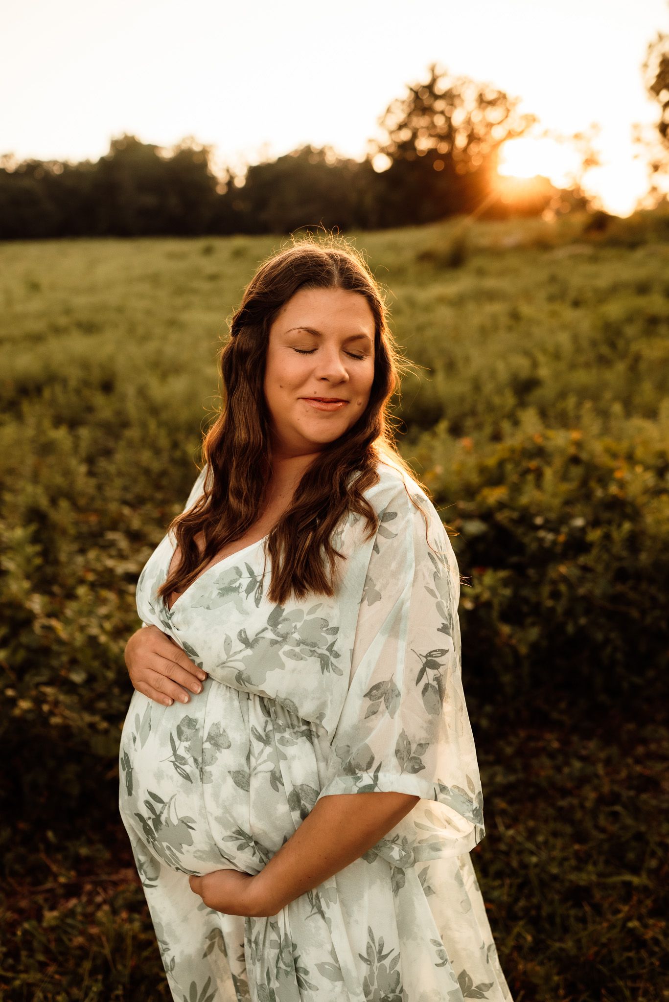 Pregnant woman holding belly in sunlit field, outdoor maternity session, Phoenixville PA