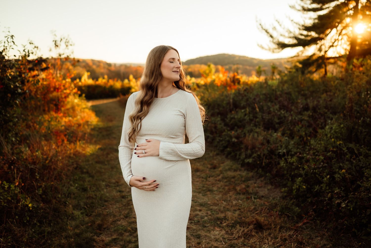 Pregnant woman holding belly in sunlit field, outdoor maternity session, Phoenixville PA