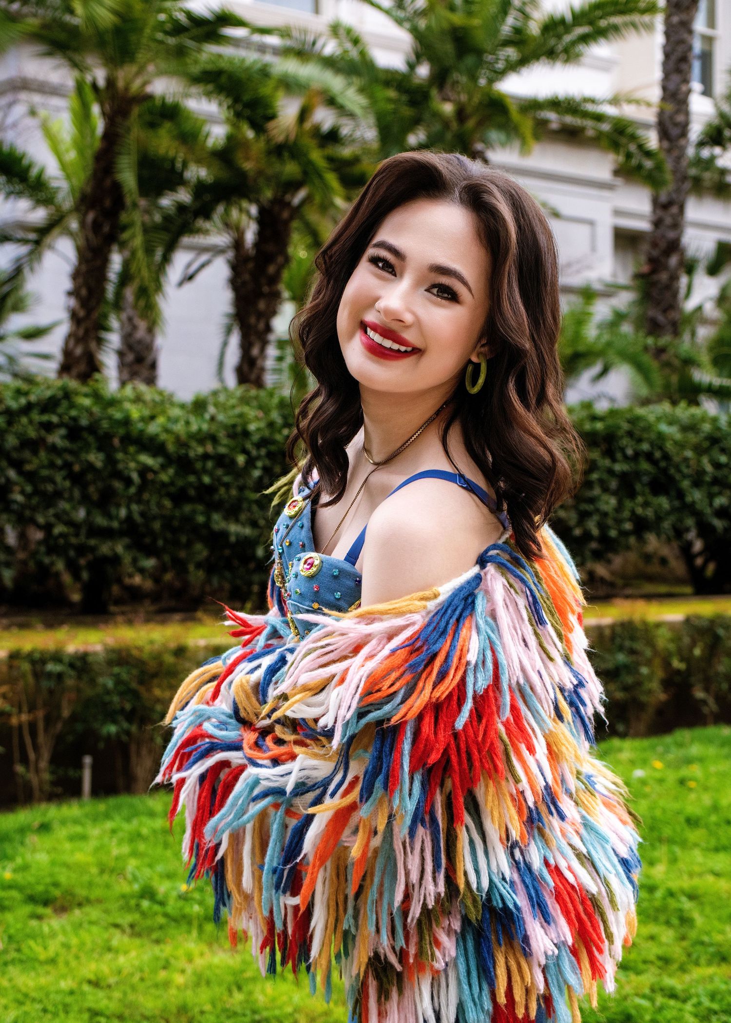 Colorful feathered dress with red, blue and white plumes creates a vibrant carnival-inspired look against a green lawn backdrop.