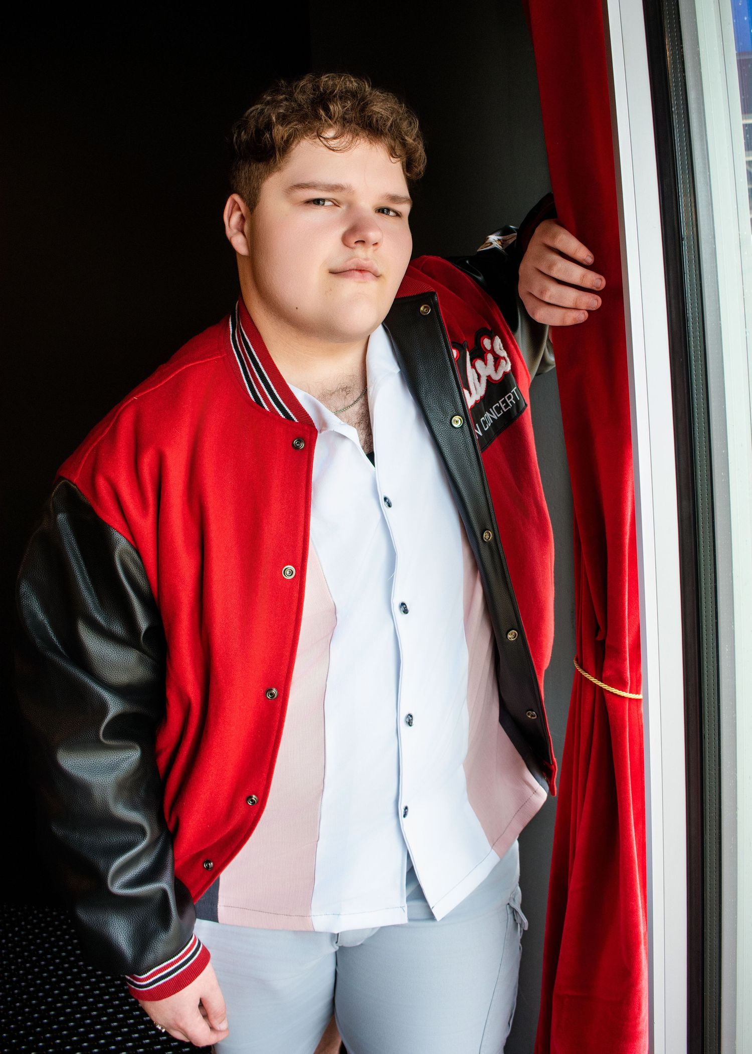 A person in a red and black varsity jacket poses against a wall with contrasting colors.