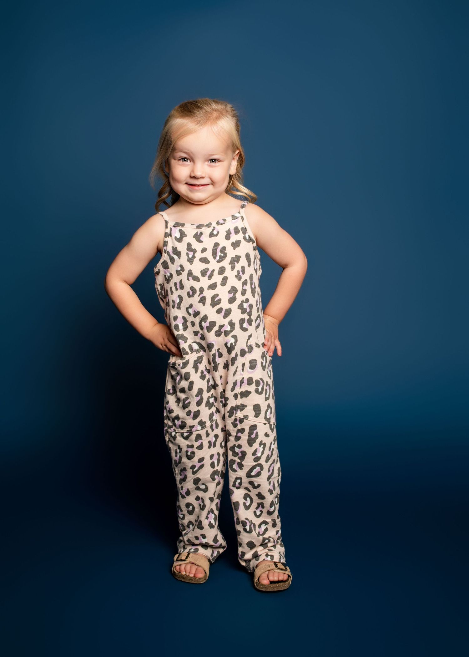 Child wearing leopard print outfit poses playfully in studio setting.