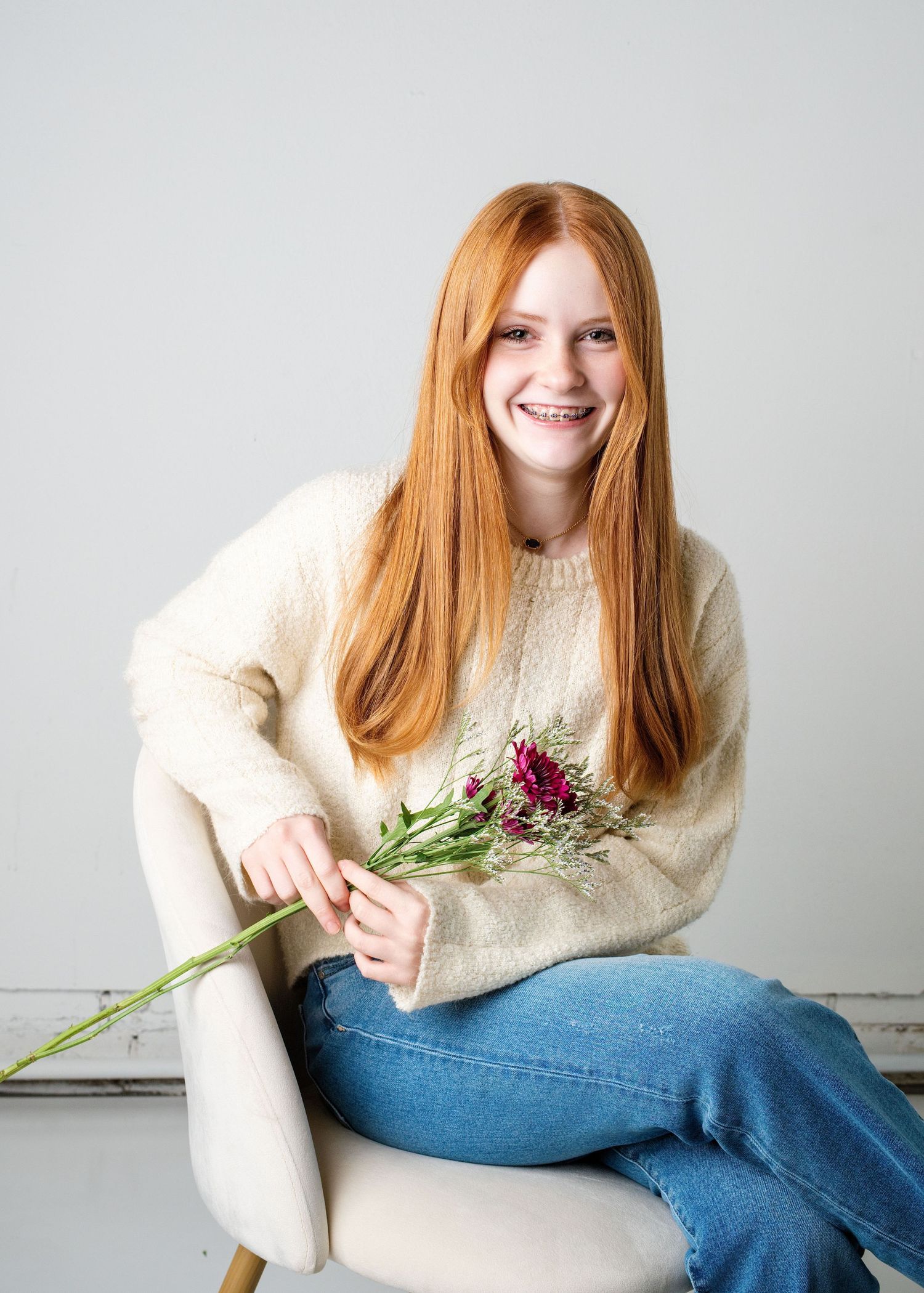 Portrait series of someone in a cream sweater and jeans posing with flowers.