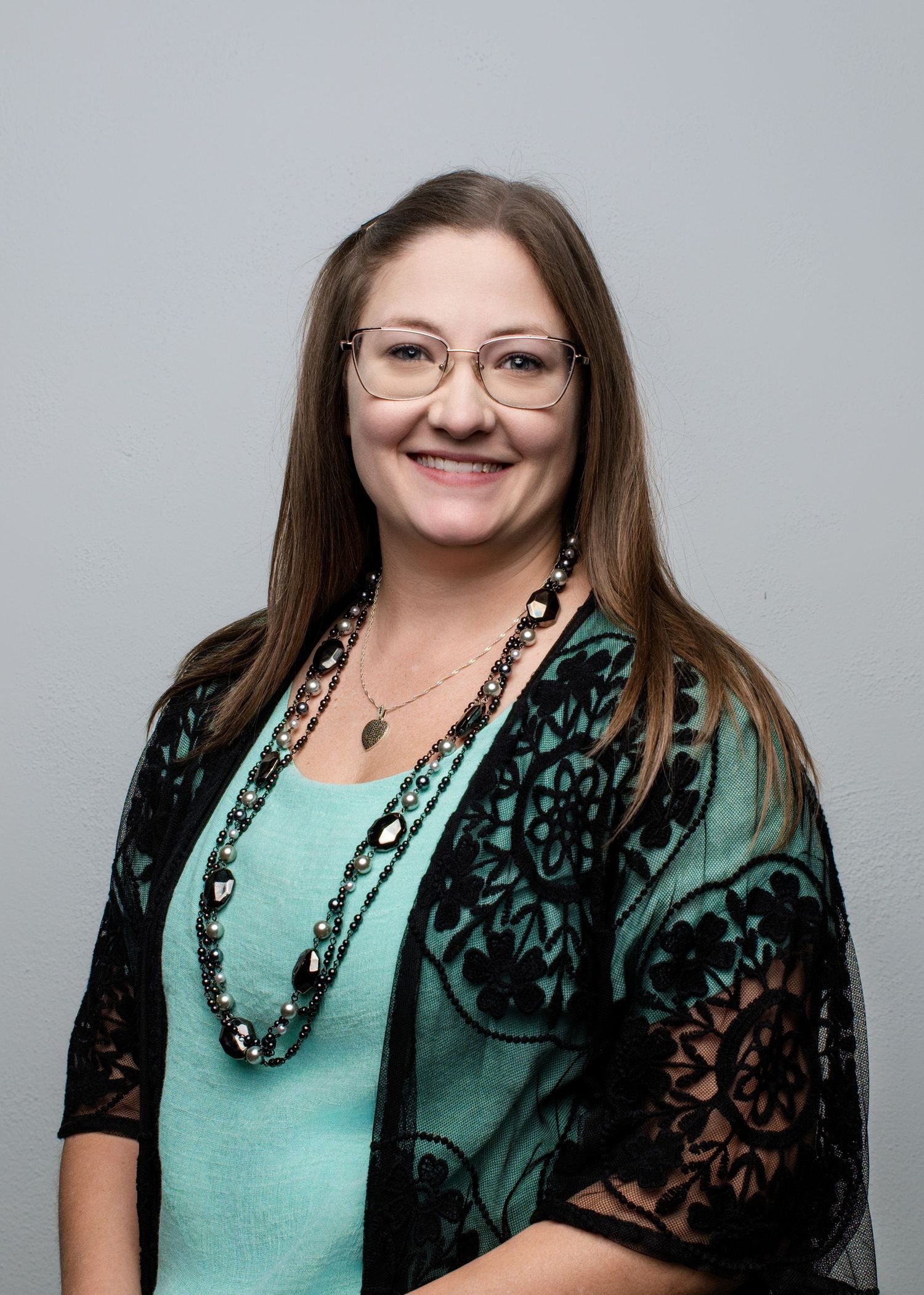 Professional headshots of someone wearing a teal top with black lace overlay.