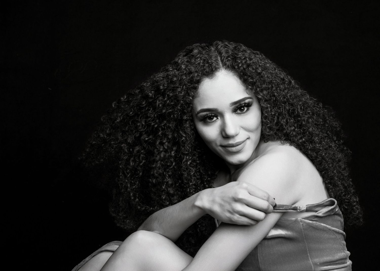 Black and white portrait of a young woman with voluminous curly hair, smiling softly in a studio setting.