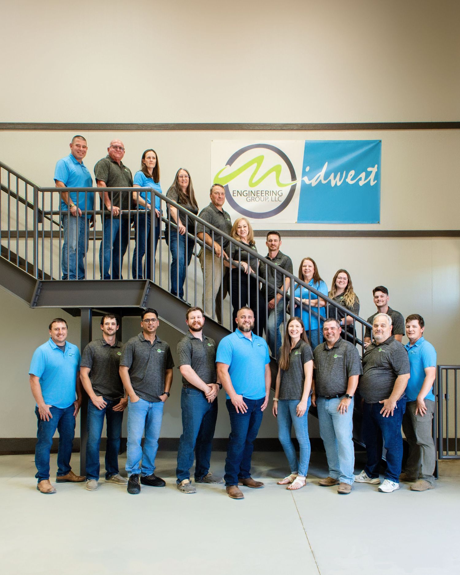 Company group photo with employees in blue shirts posed on office staircase.
