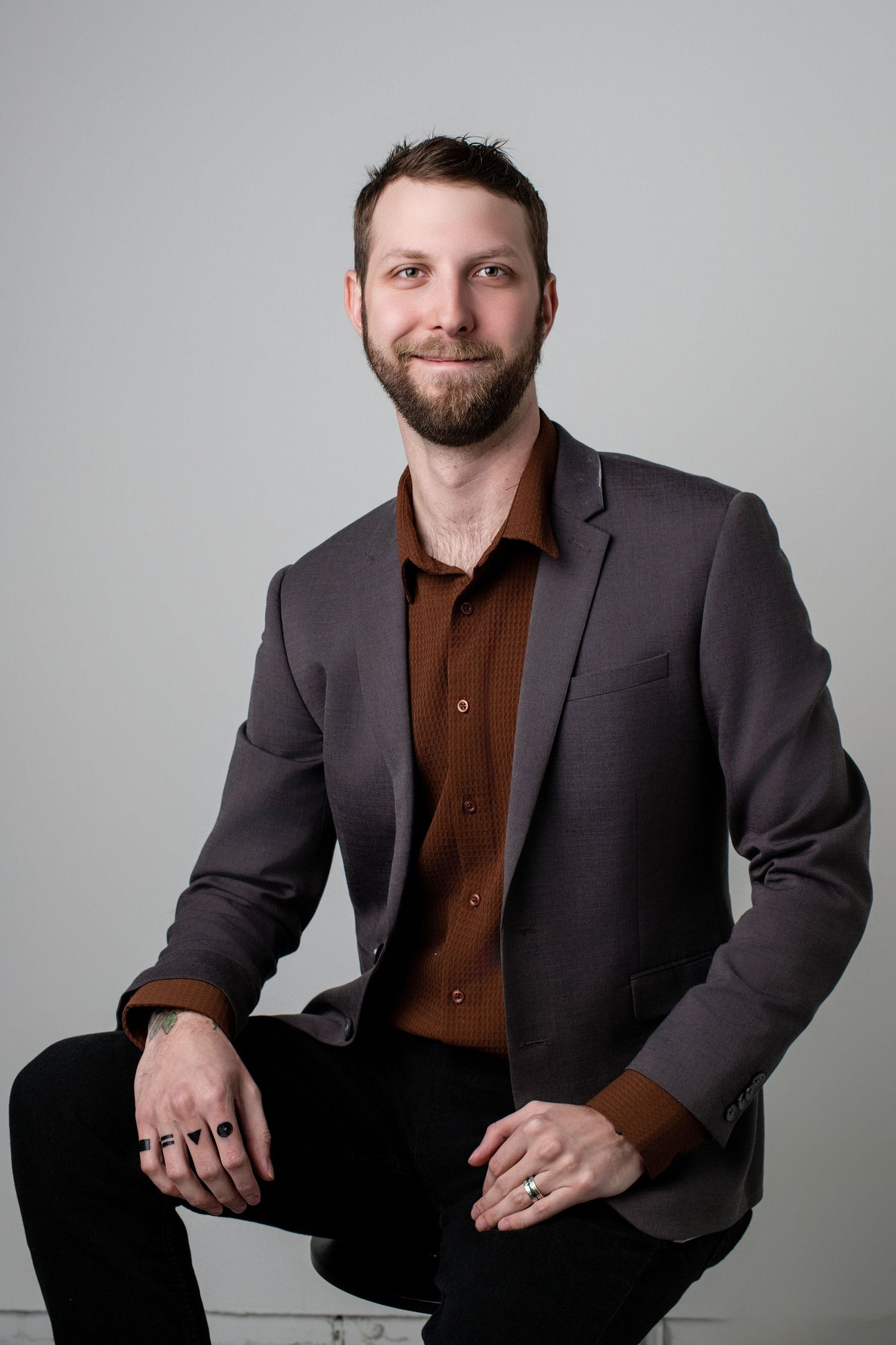 Professional headshots of a person in a dark suit jacket and brown shirt against a gray background.