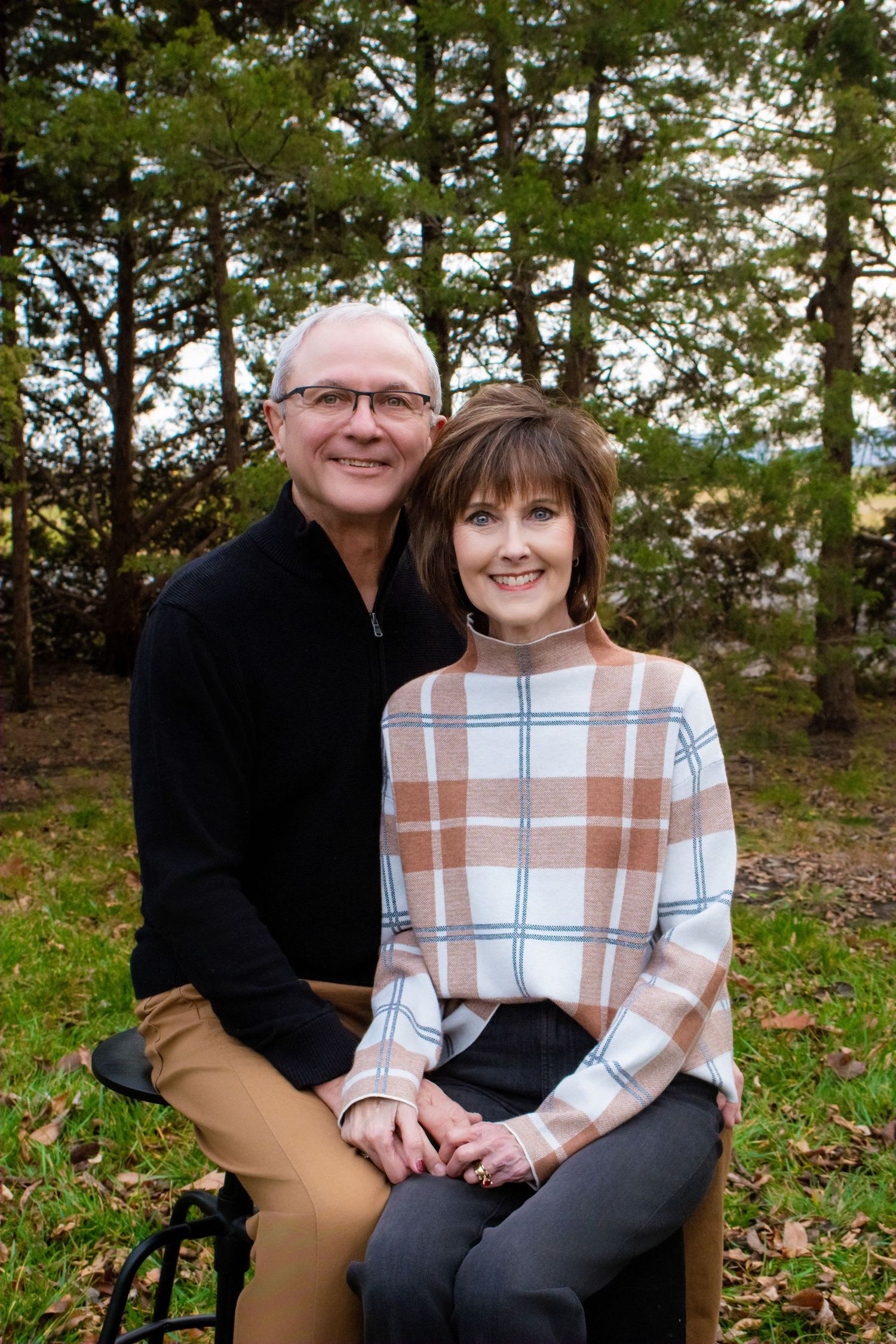 Couple's outdoor portrait session among pine trees in casual attire.