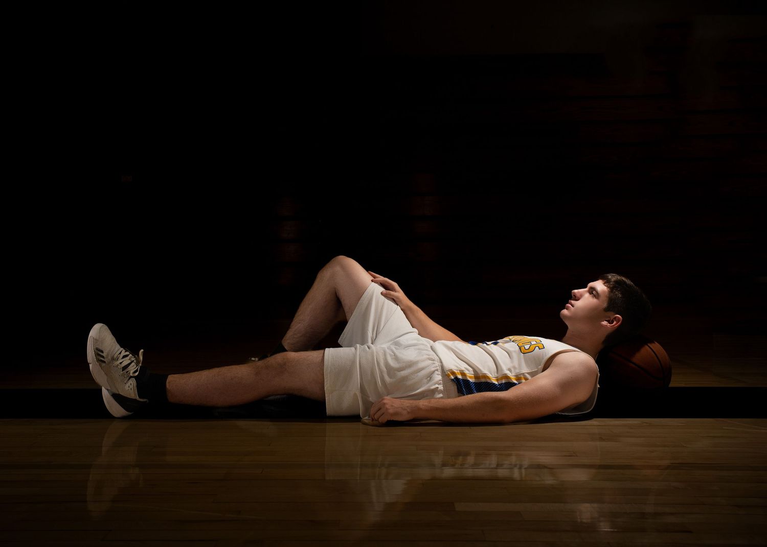 Dramatic low-light portrait of someone lying on a wooden floor and a basketball.