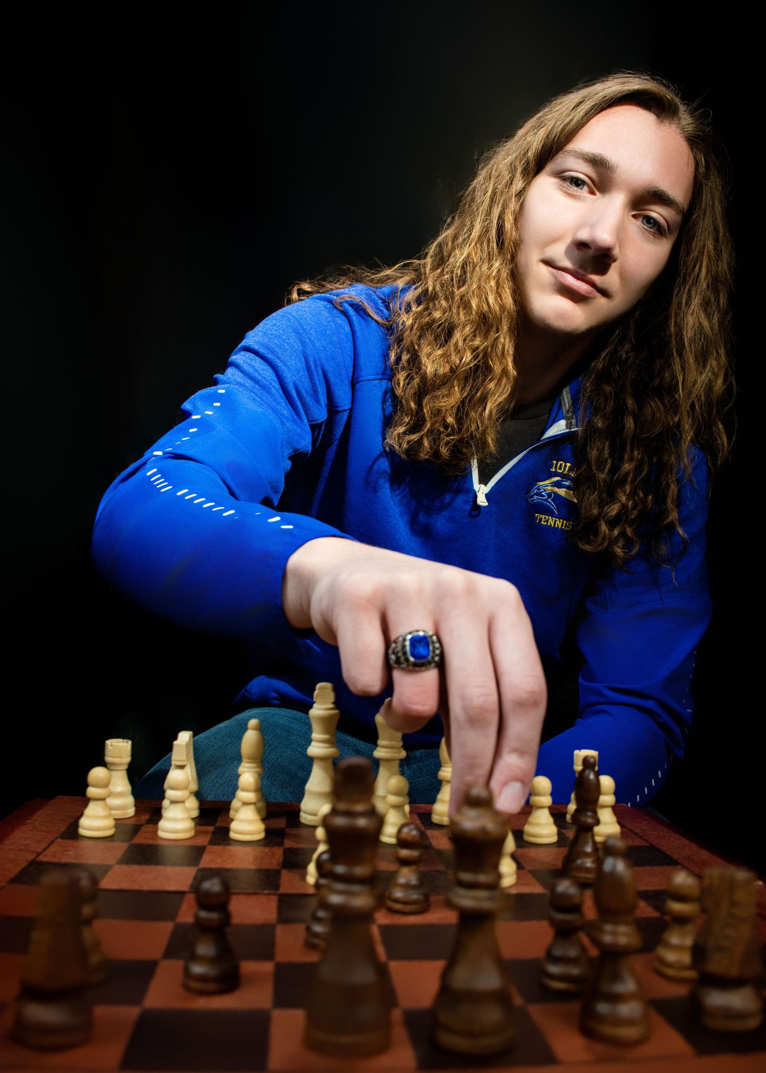 Chess player in blue jacket making a move on wooden chess board in dramatic lighting.