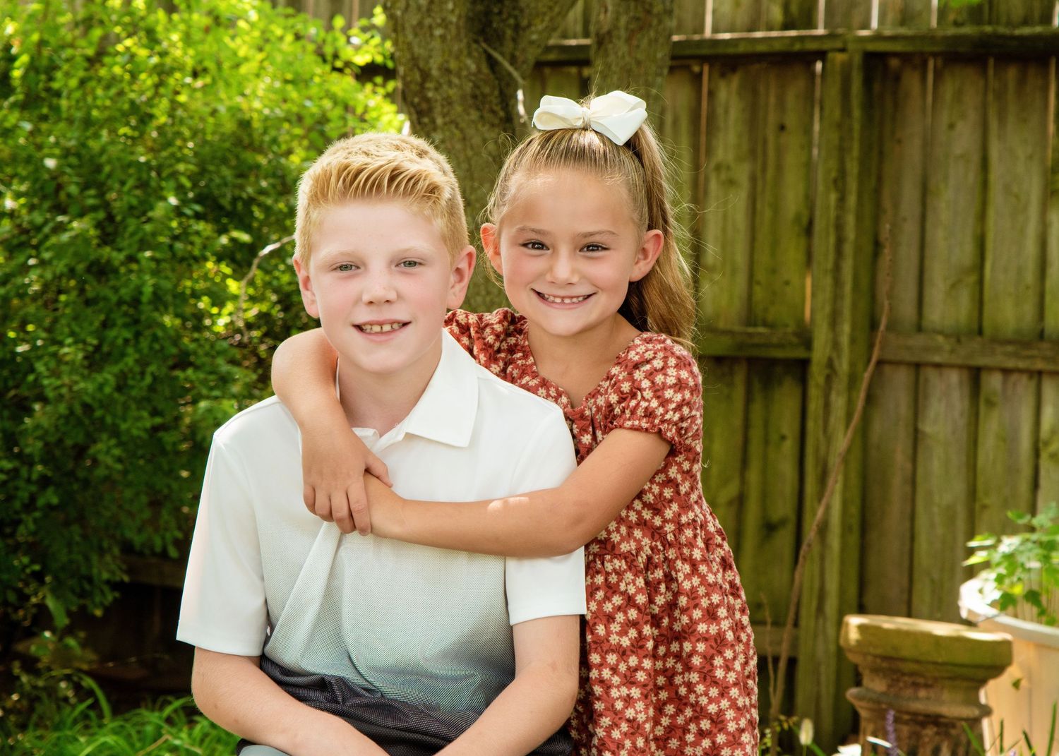 Casual outdoor family photo session with wooden fence and greenery backdrop.